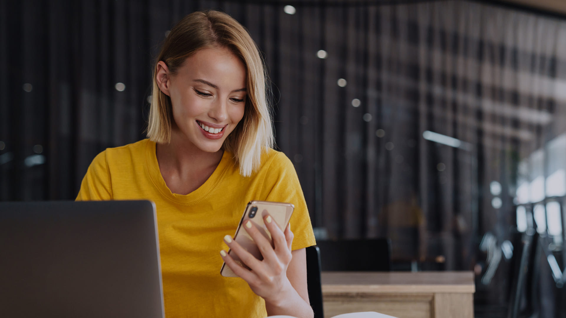 Smiling woman using smartphone and laptop.